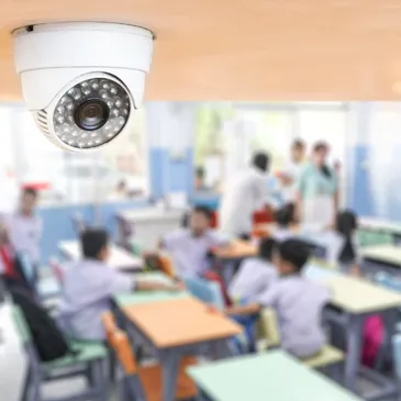 Ceiling-mounted security camera with infrared lights in a classroom setting.